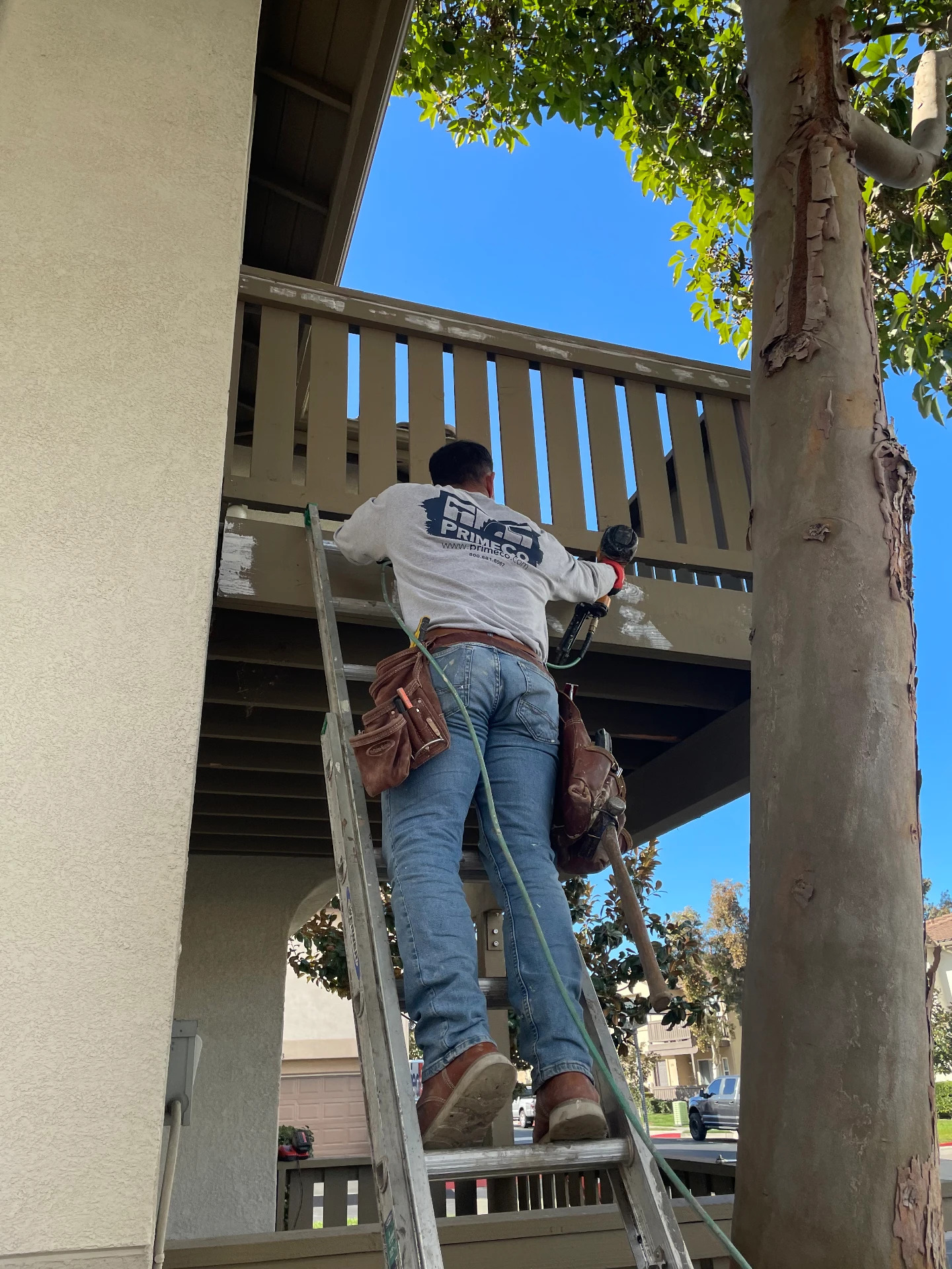 PrimeCo crew member refinishing an exterior stair railing from a ladder