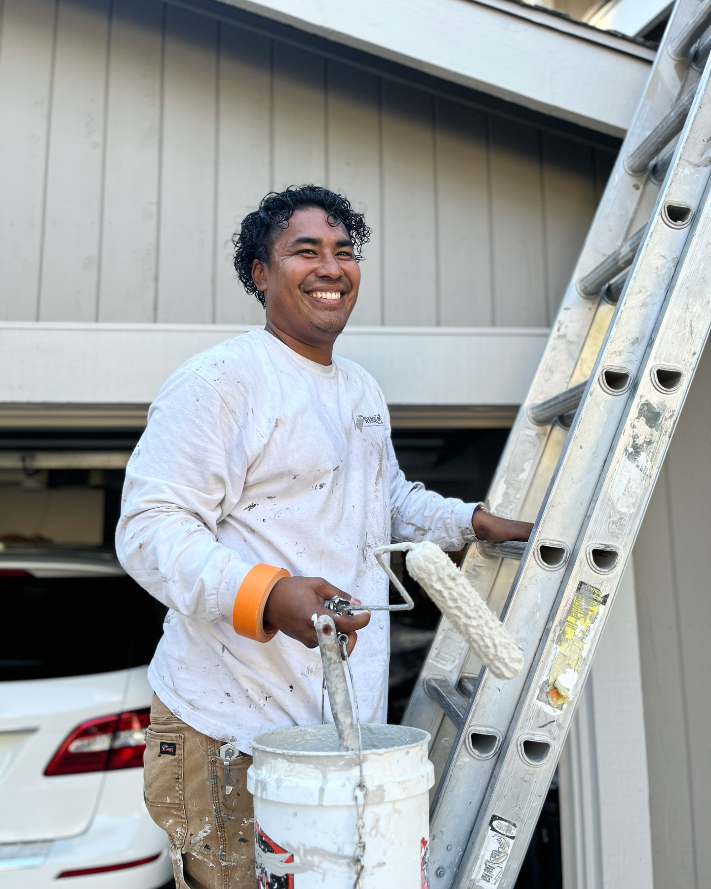 PrimeCo painter smiling on the job site with a roller and ladder
